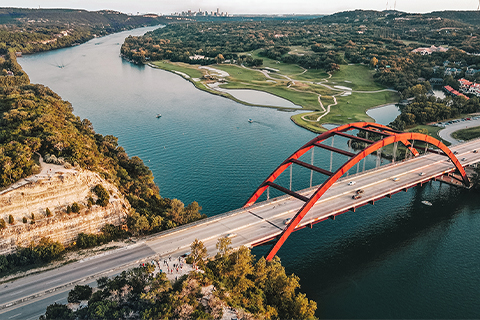 Zdjęcie z lotu ptaka, na którym widać rzekę i most w Austin w stanie Teksas, a w tle także samo miasto.