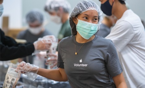 Una becaria de Apple con una camiseta de voluntariado, sonríe y ve hacia un lado mientras empaca artículos en un evento.