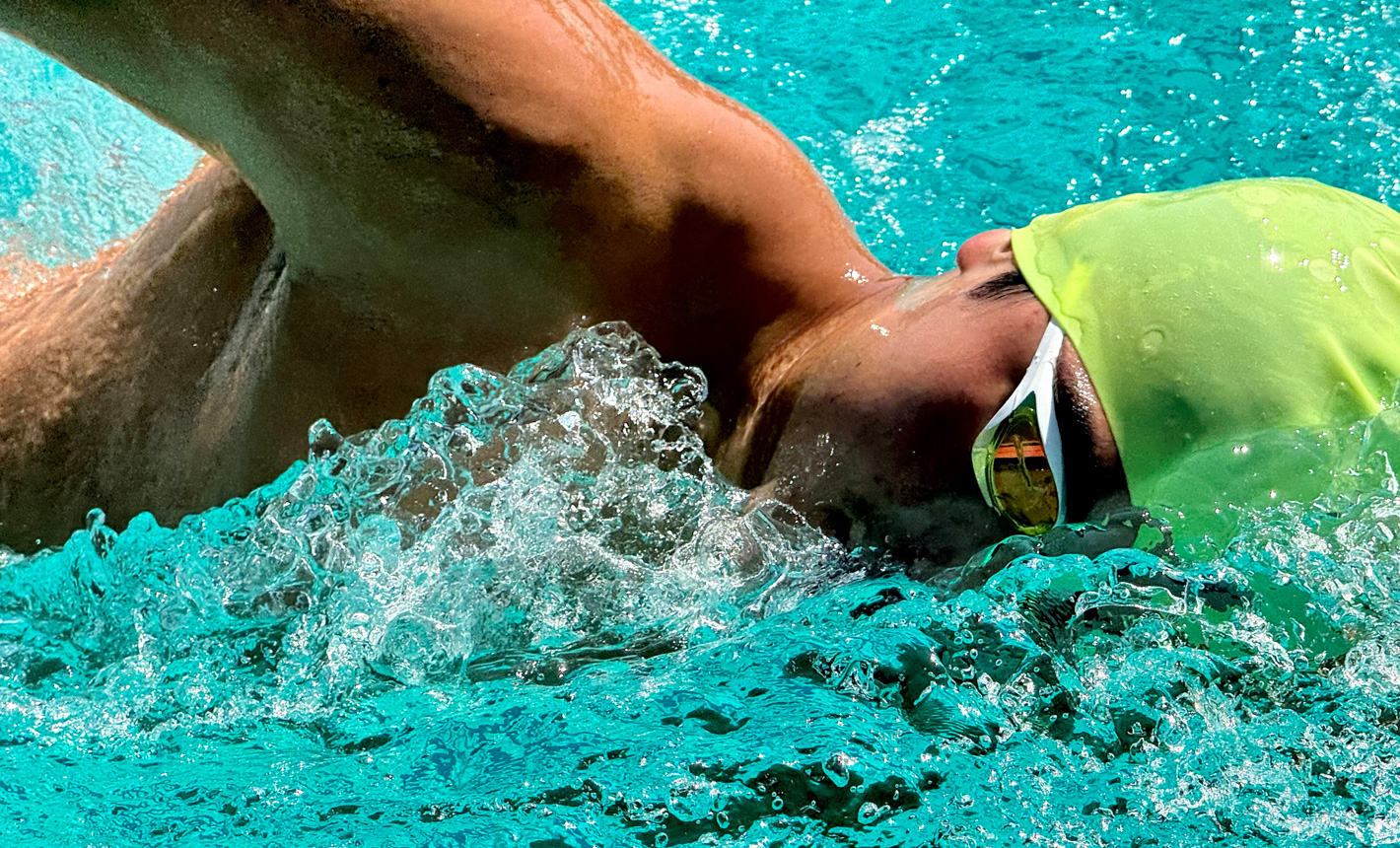 ภาพซูมที่มีรายละเอียดสูงของนักว่ายน้ำคนหนึ่งในสระโดยมีน้ำกระเซ็นอยู่รอบๆ ตัว