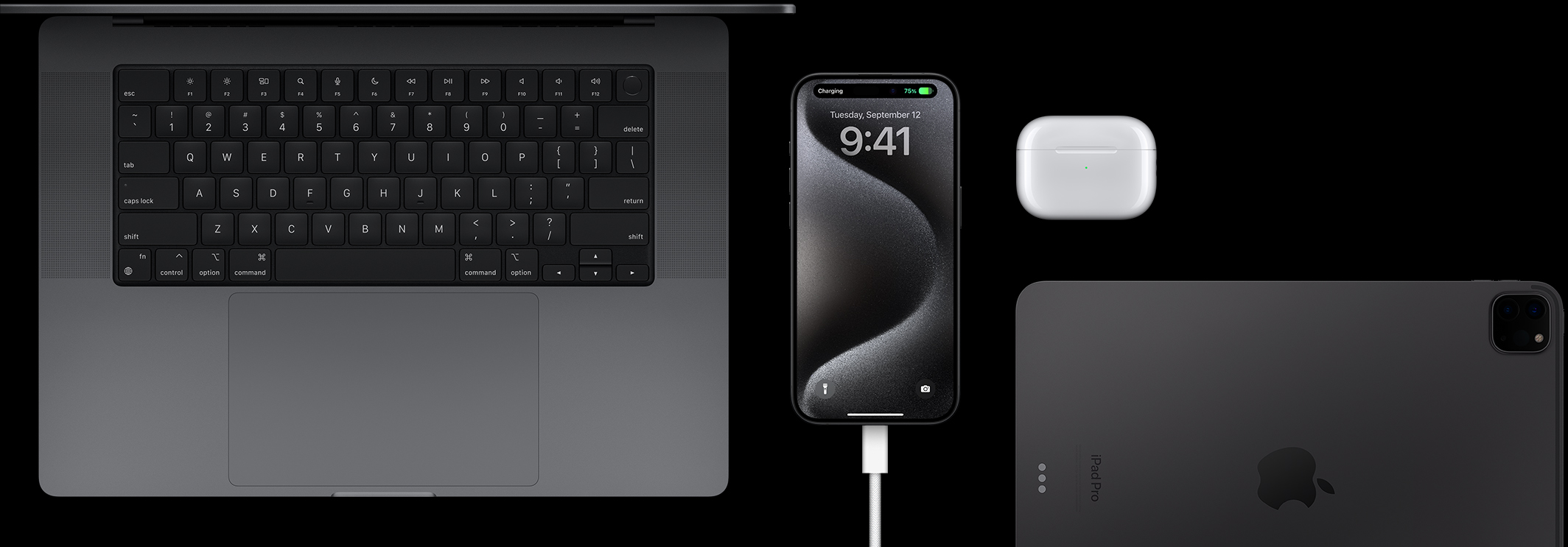 iPhone 15 Pro, johon on liitetty USB‑C-johto ja jota ympäröivät MacBook Pro, AirPods Pro ‑kuulokkeet ja iPad