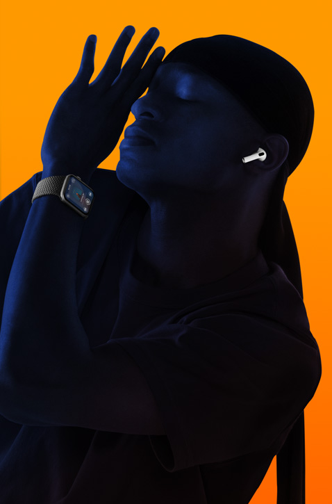 A person listening to music on an Apple Watch wearing AirPods, with their eyes closed and leaning back with their hand raised toward their face.
