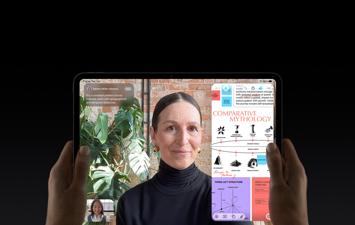 iPad Pro, front exterior, space black colour, left and right hands holding in landscape orientation, rounded corners, black display bezel, display showing a FaceTime conversation being live translated, and an educational app showing a presentation of ‘Comparative Mythology’ with text, diagrams and handwritten notes