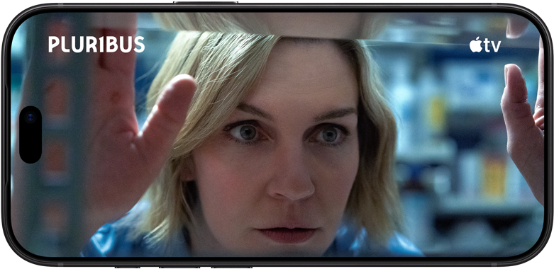 iPhone 18 Pro, хоризонтален, показва близък план на жена, която гледа през рафт. Заглавие на сериала: Pluribus