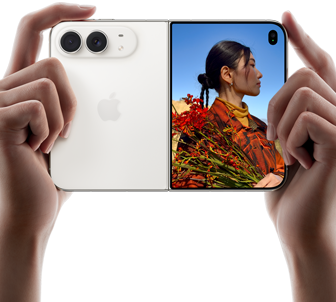 iPhone Duo, звездно бяло, държан в две ръце в хоризонтална ориентация, разгънат, левият панел показва 48MP Dual Fusion задни камери, а десният панел показва човек, когото снимат на външния дисплей, обектът на снимката вижда лицето си, докато го снимат с Duo Preview