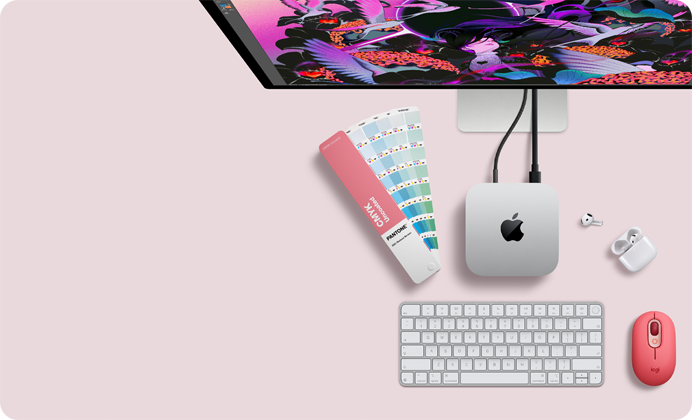 Mac mini, отгоре, сребърен алуминий, заоблени ъгли, гланцирано черно лого на Apple в центъра, свързано с кабел, Studio Display е частично видим отгоре, AirPod 4, отворени, Pantone цветови мостри и цифрова клавиатура, и мишка