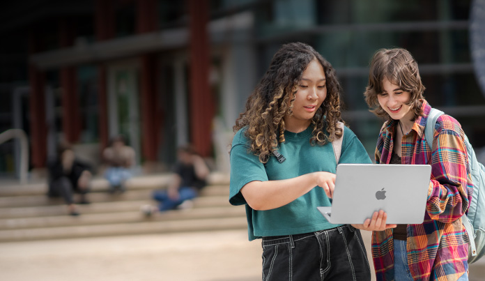 Duas estudantes universitárias olham para a tela de um MacBook no campus