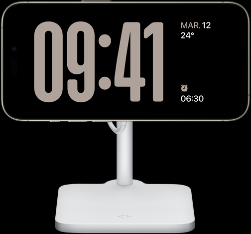 An iPhone 15 Pro in StandBy showing a full-screen clock along with the date, the temperature, and the next alarm