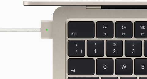 Vue en plongée d’un MacBook Air comète auquel est branché un câble MagSafe de la même couleur