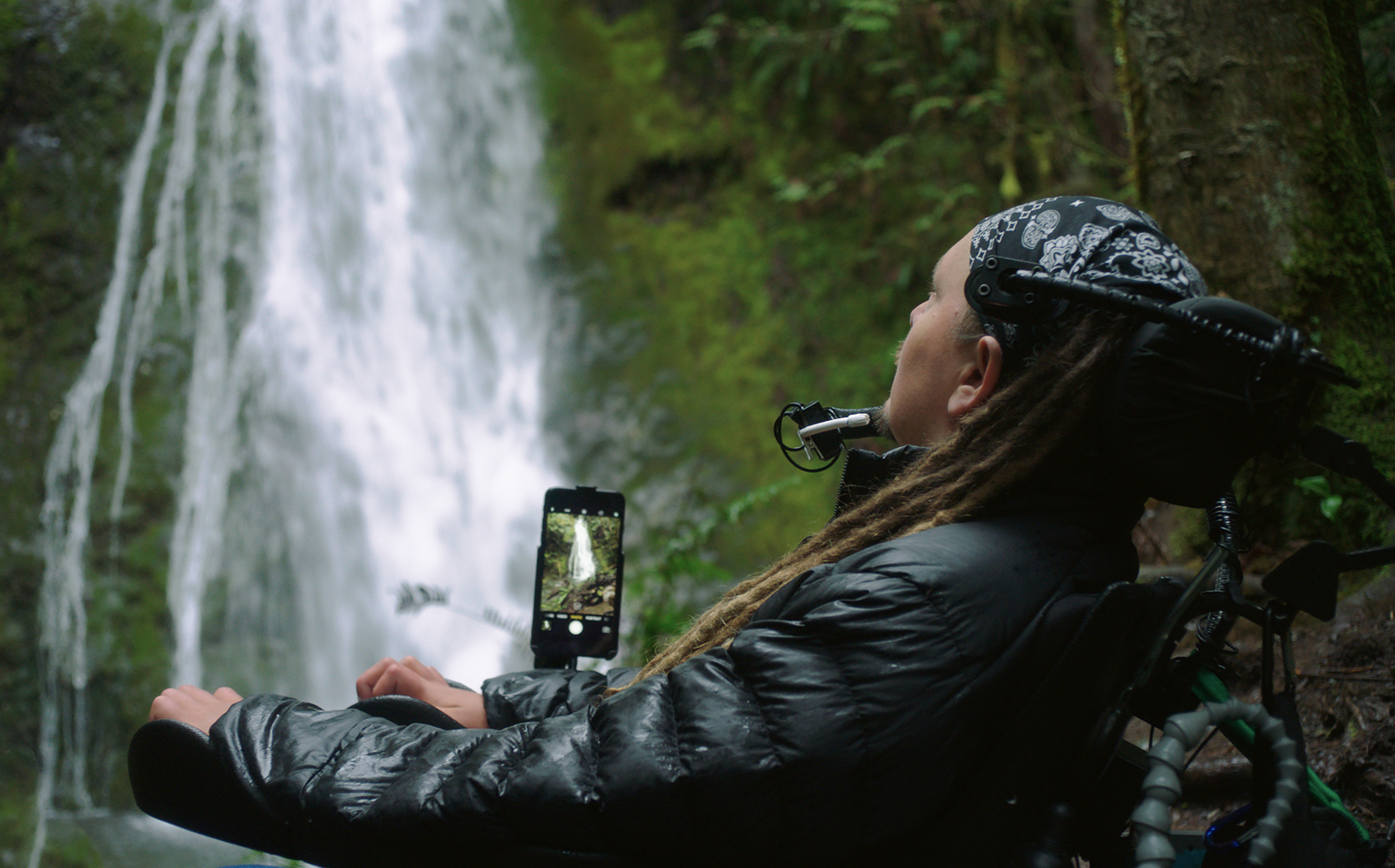 In front of a waterfall, a man in a wheelchair uses Switch Control assistive technology to operate his iPhone camera.