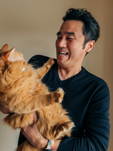 Fotoportræt af Tetsu, der holder og ser på sin kat, mens han smiler.