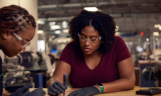 A Camara e uma colega usam óculos de proteção enquanto trabalham juntas numa estação de laboratório.