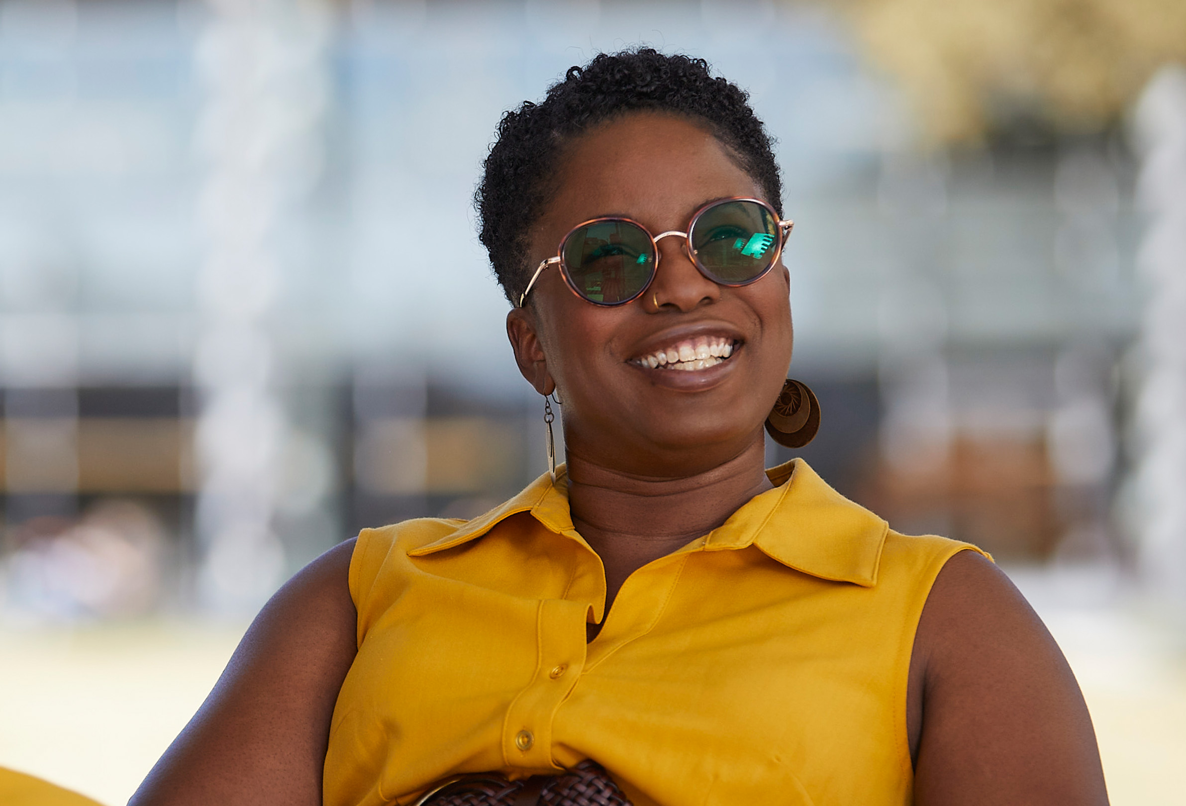 Una empleada de Apple sonríe y está sentada en el exterior con lentes de sol puestos.