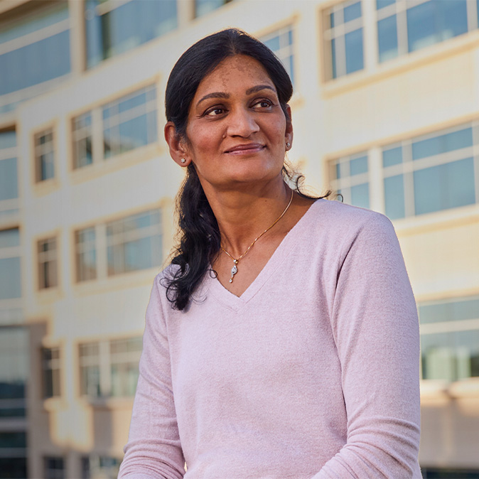 Ramani sentada afuera de un edificio de oficinas, sonríe y mira hacia un lado.