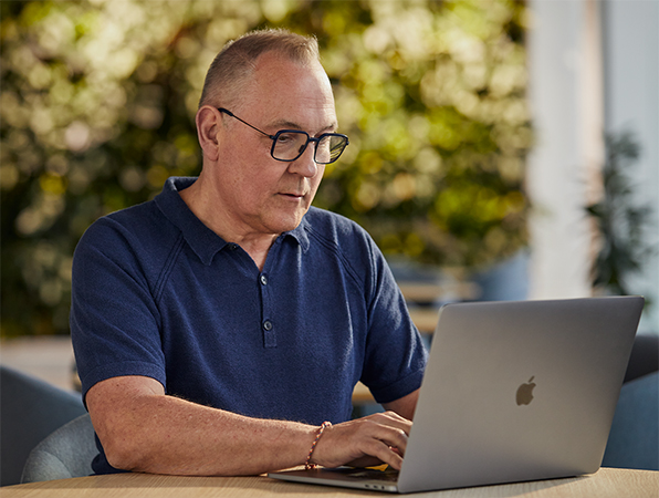 En ansatt på Apples team for programvare og tjenester jobber utendørs på en MacBook med et grøntområde i bakgrunnen.