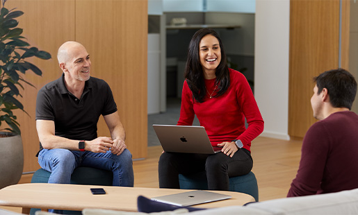 Camila két Apple-munkatársa között ül nevetve, MacBookkal az ölében.