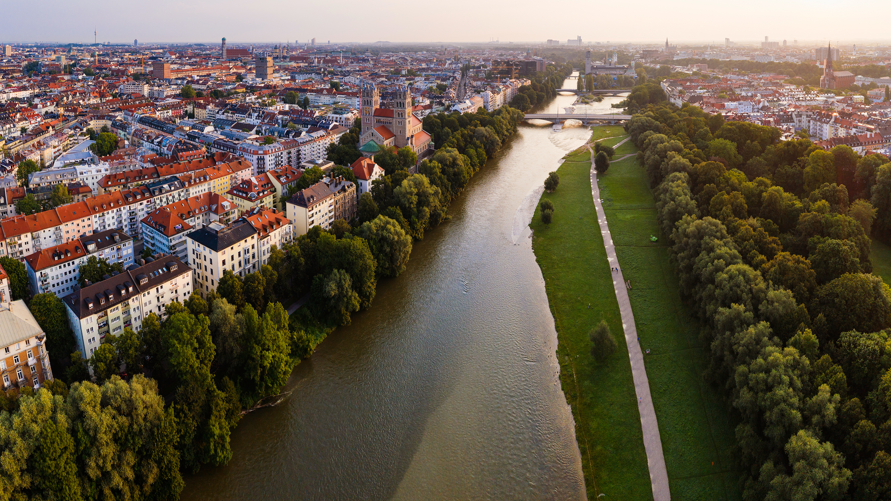 Aerial view of Munich with a river, trees, and a walking path alongside the river.
