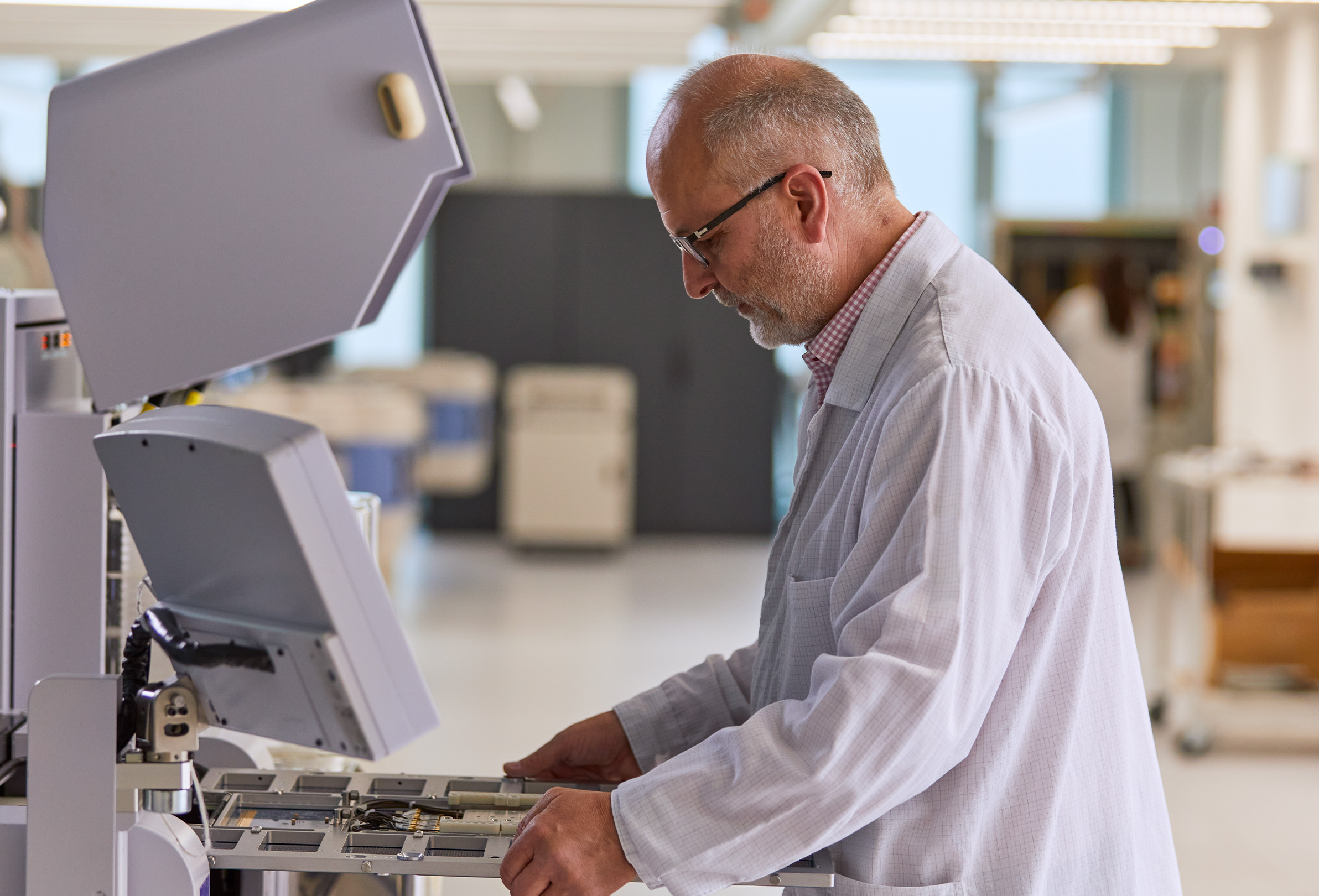 An Apple employee wearing a white lab coat and working on engineering equipment. 