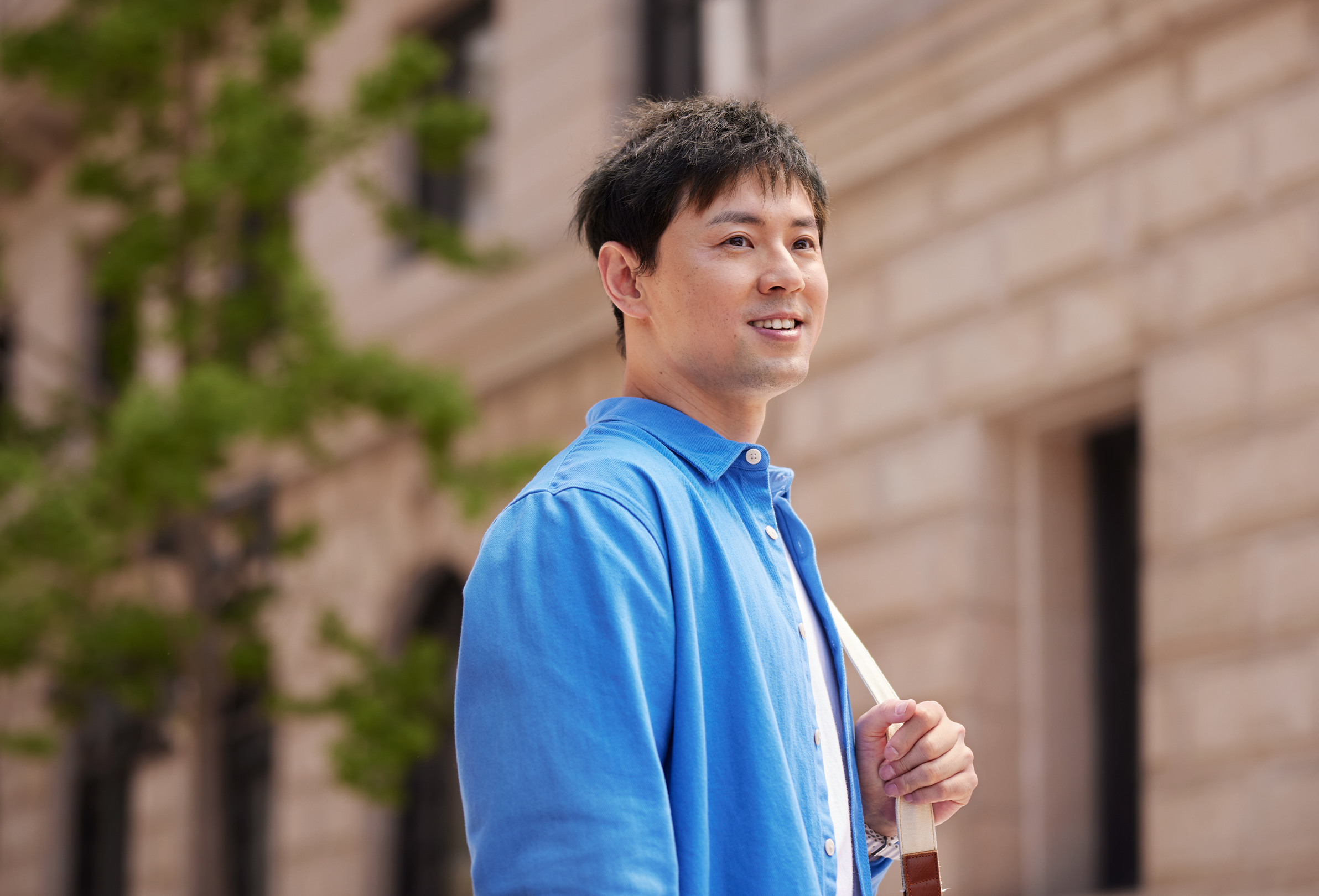 Een glimlachende Apple medewerker staat buiten een stenen kantoorgebouw met een schoudertas om.