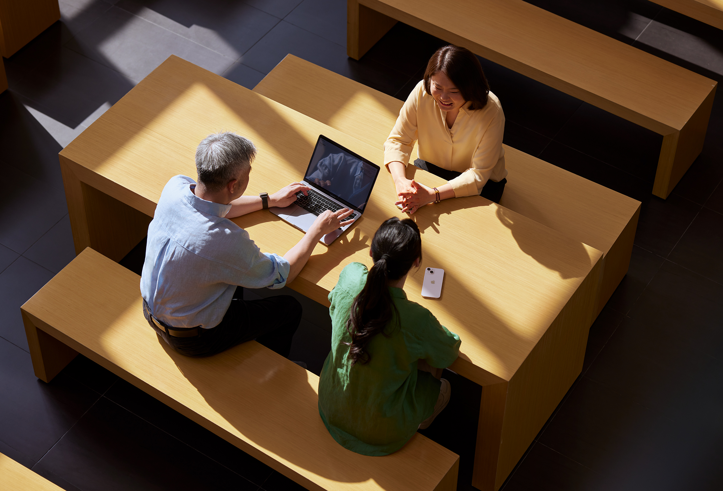 Tres empleados de Apple sentados juntos mientras uno trabaja en una MacBook.