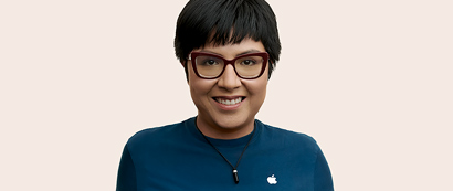 Apple Retail Mitarbeiterin mit kurzen Haaren und Brille lächelt in die Kamera.