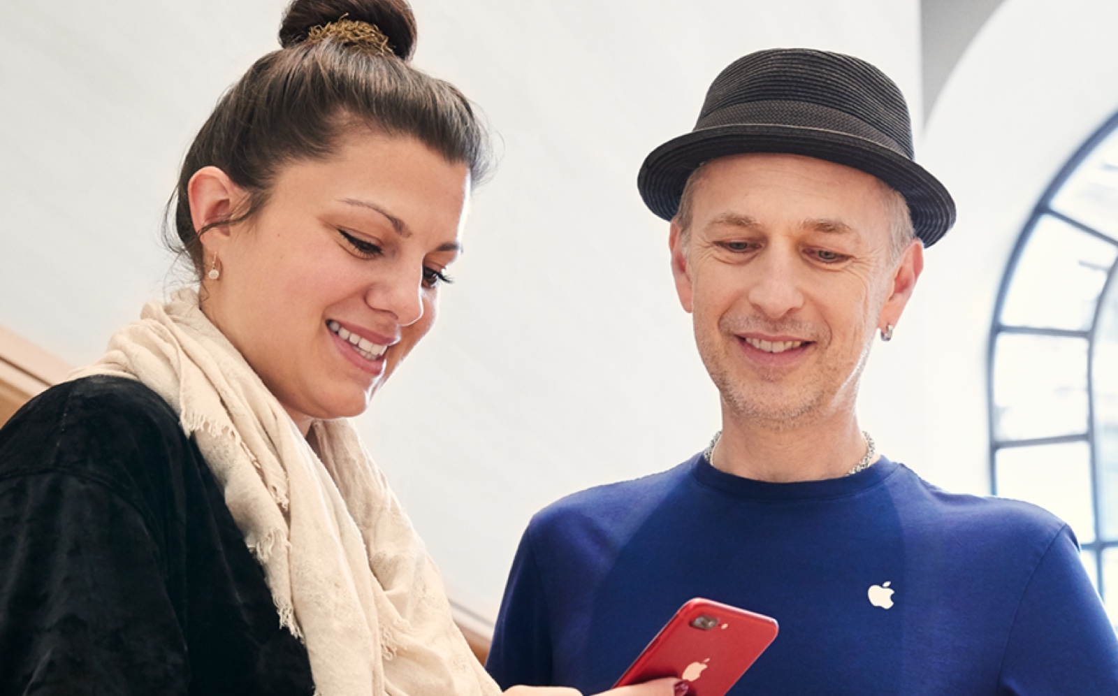 In an Apple Store, a male employee helps a customer use features on her iPhone.