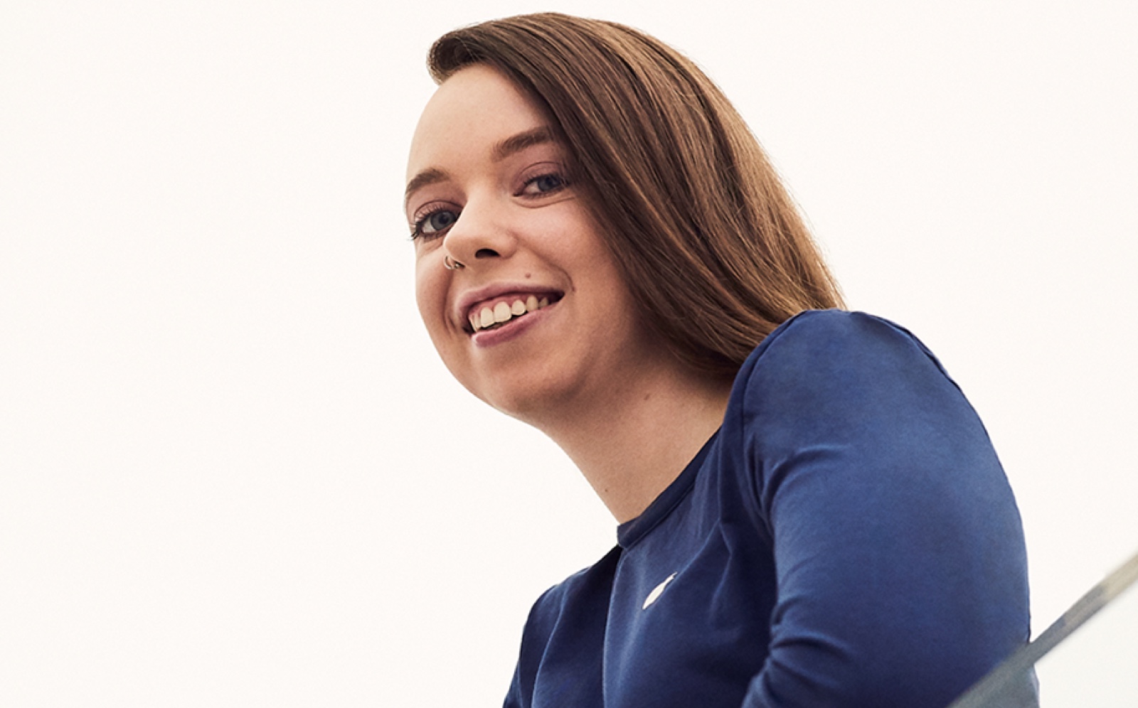 In an Apple Store, a female employee leans over a banister, smiling.