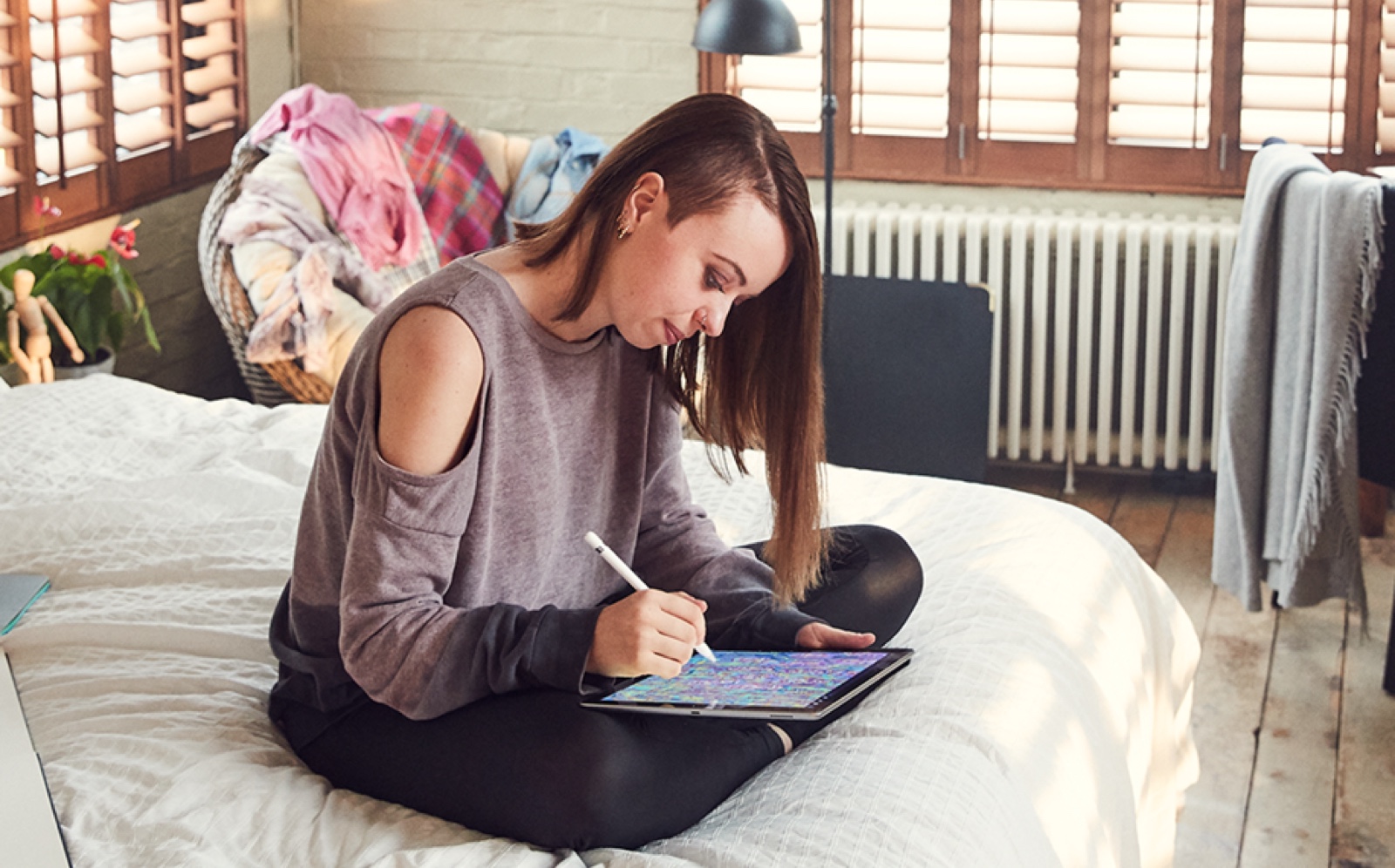 自宅のベッドに座ってApple PencilとiPadで絵を描くApple Storeの女性スタッフ。