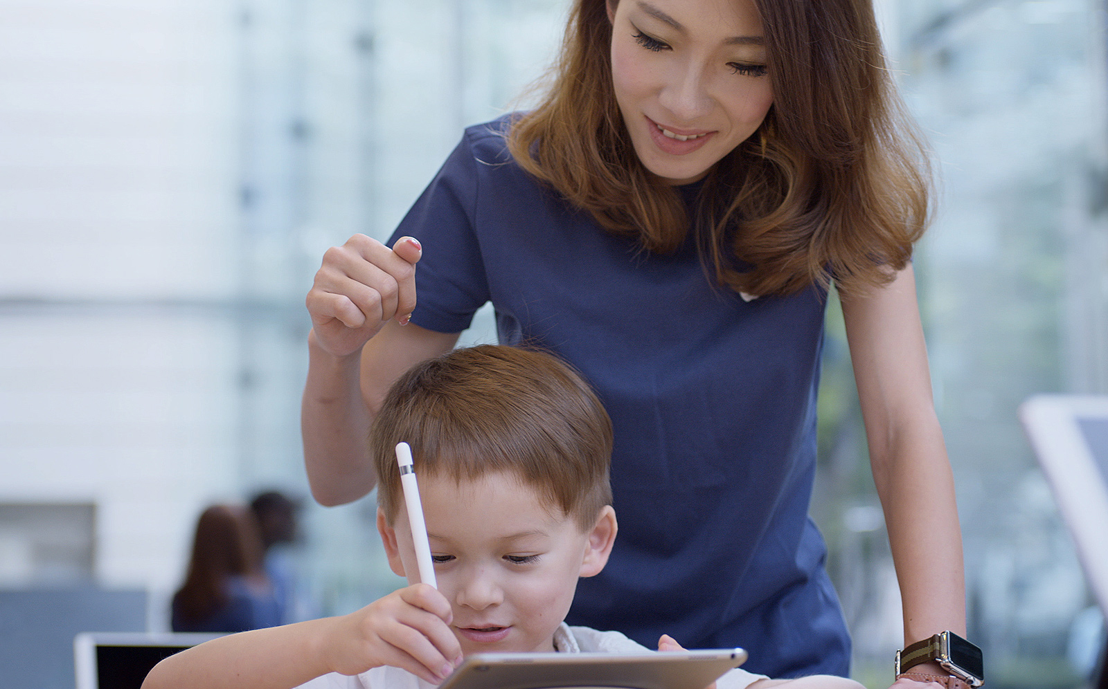 Apple PencilでiPadに絵を描いている少年を、背後からサポートしているApple Storeの女性スタッフ。
