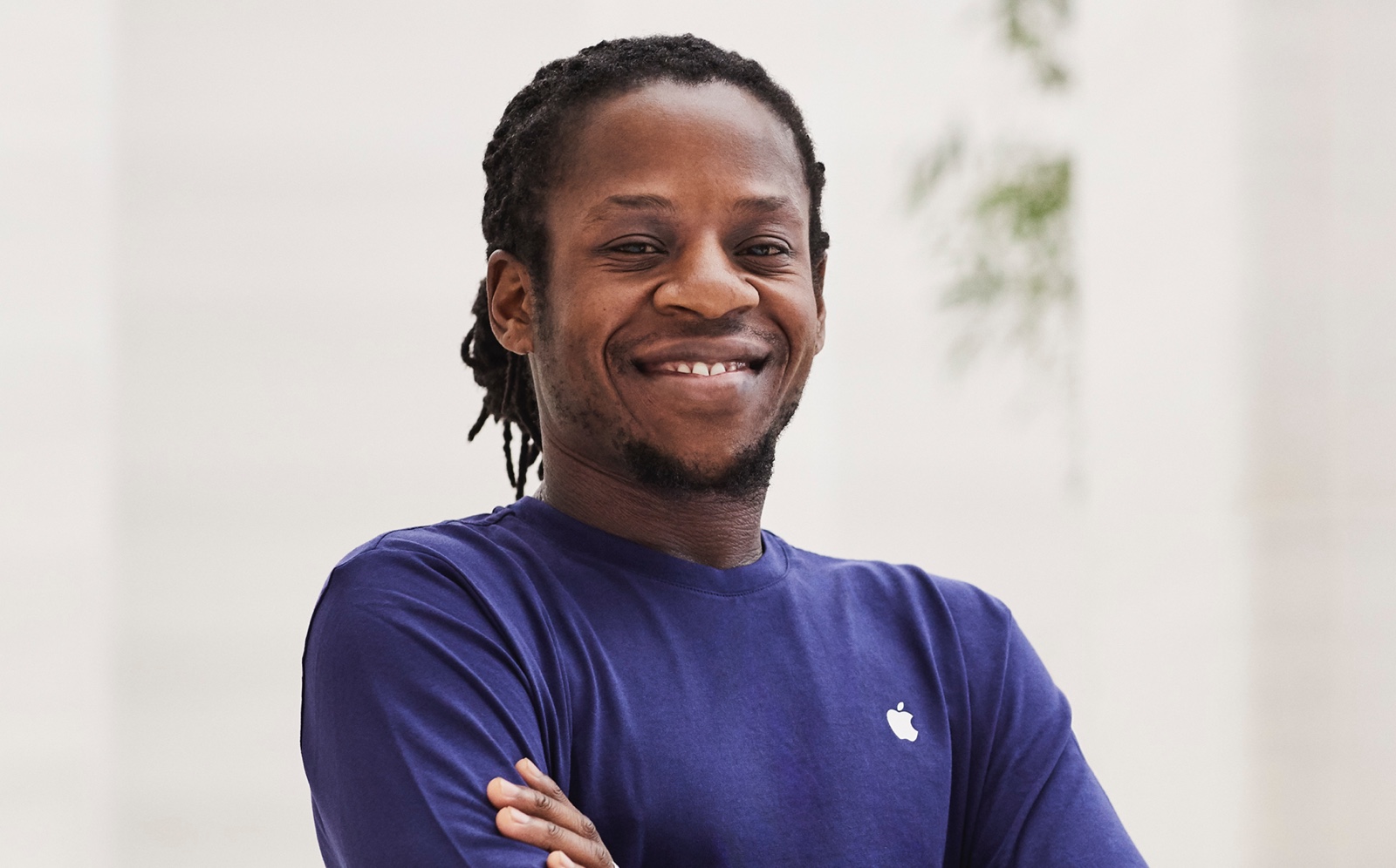 A male Apple Store employee stands in the store, looking into the camera and smiling.