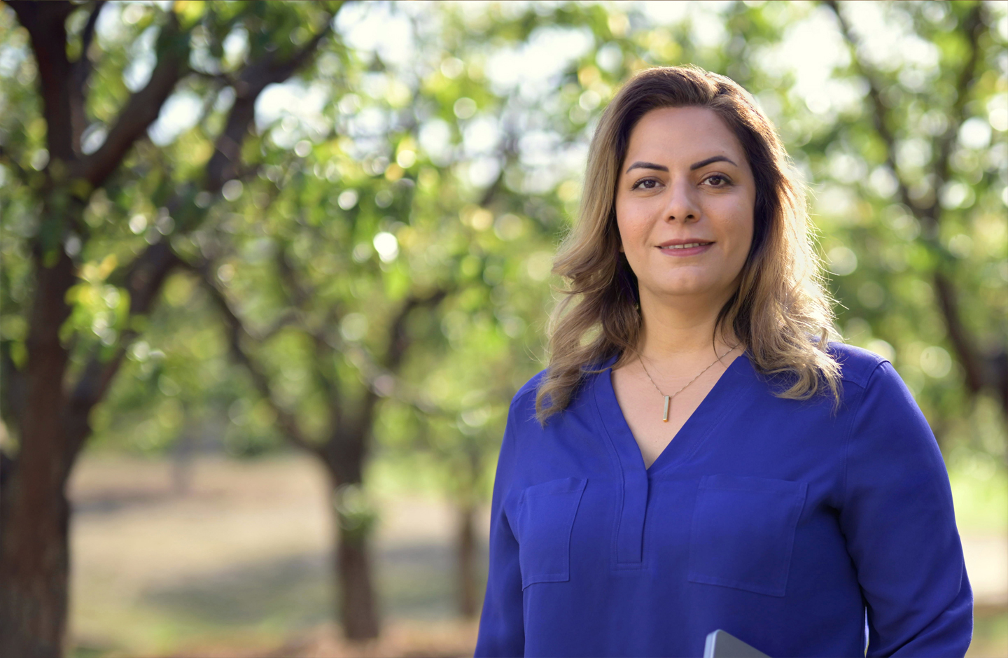 Desireh, de pie, sostiene una MacBook, sonríe a la cámara