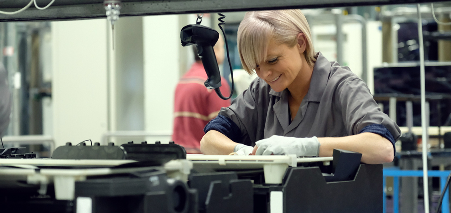 在一家 Apple 製造廠中，兩名員工正在鈦合金陽極機架上檢查 MacBook 鋁金屬外殼