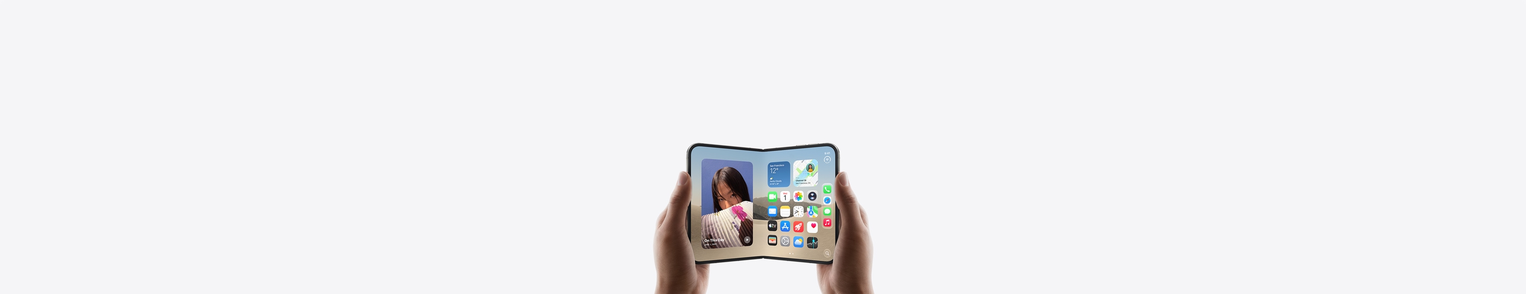 Otevřený iPhone Duo je otočený na šířku a drží ho dvě ruce, na vnitřním displeji je vidět plocha