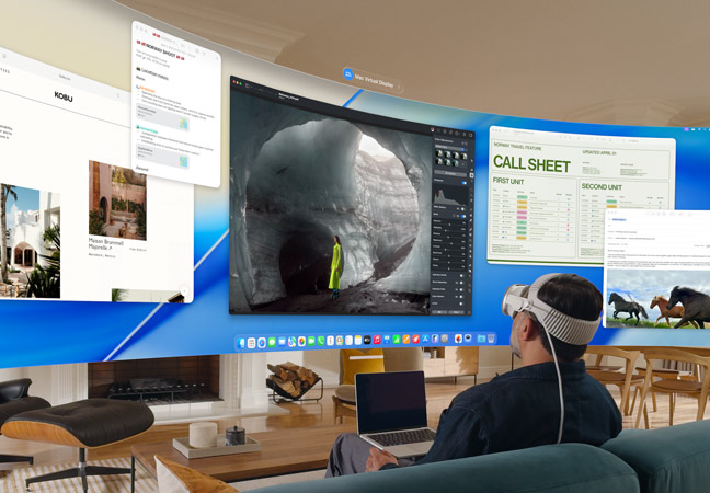 Person wearing Apple Vision Pro sits on a couch in a living room with an open MacBook on lap, ultrawide screen Mac Virtual Display floats in front of the person, filling the room