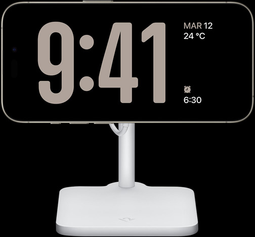 Un iPhone 15 Pro en modo En Reposo que muestra el reloj a pantalla completa junto con la fecha, la temperatura y la siguiente alarma