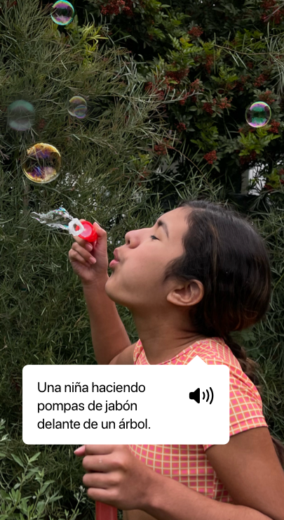 VoiceOver dice qué aparece en una foto y muestra el texto de la descripción: «Una niña haciendo pompas de jabón delante de un árbol.»