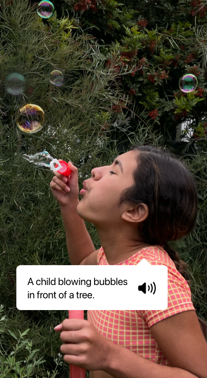 VoiceOver describing a photo and showing speech output. ‘A child blowing bubbles in front of a tree.’
