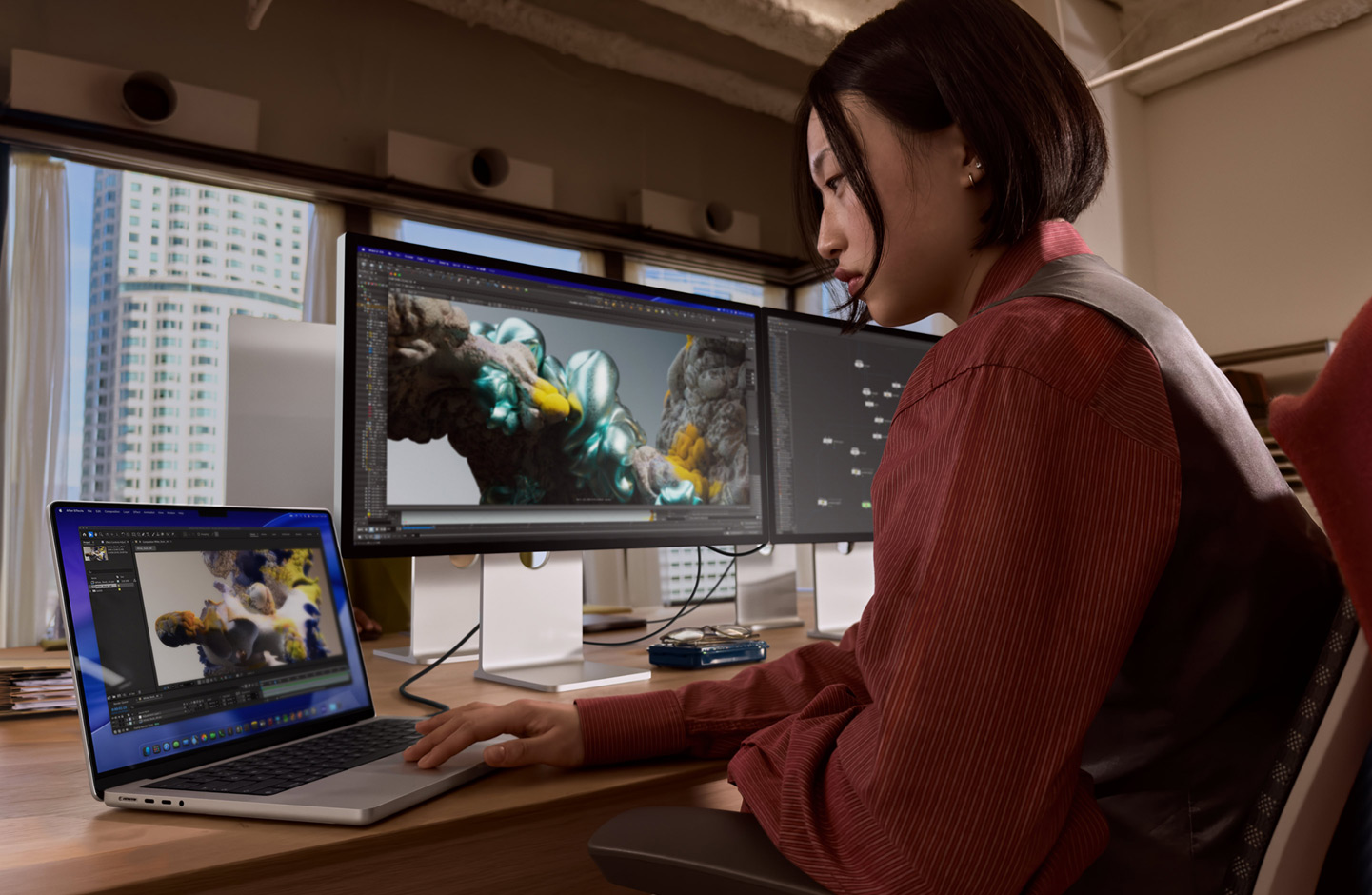 Iemand die op kantoor werkt op een MacBook-laptop die via een Thunderbolt 5-poort is verbonden met een Studio Display XDR