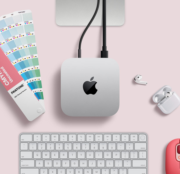 俯視圖展示銀色 Mac mini 擺放在桌上,旁邊放有 AirPods、一個粉紅色無線鍵盤、粉紅色無線滑鼠,以及一疊扇狀顏色卡。