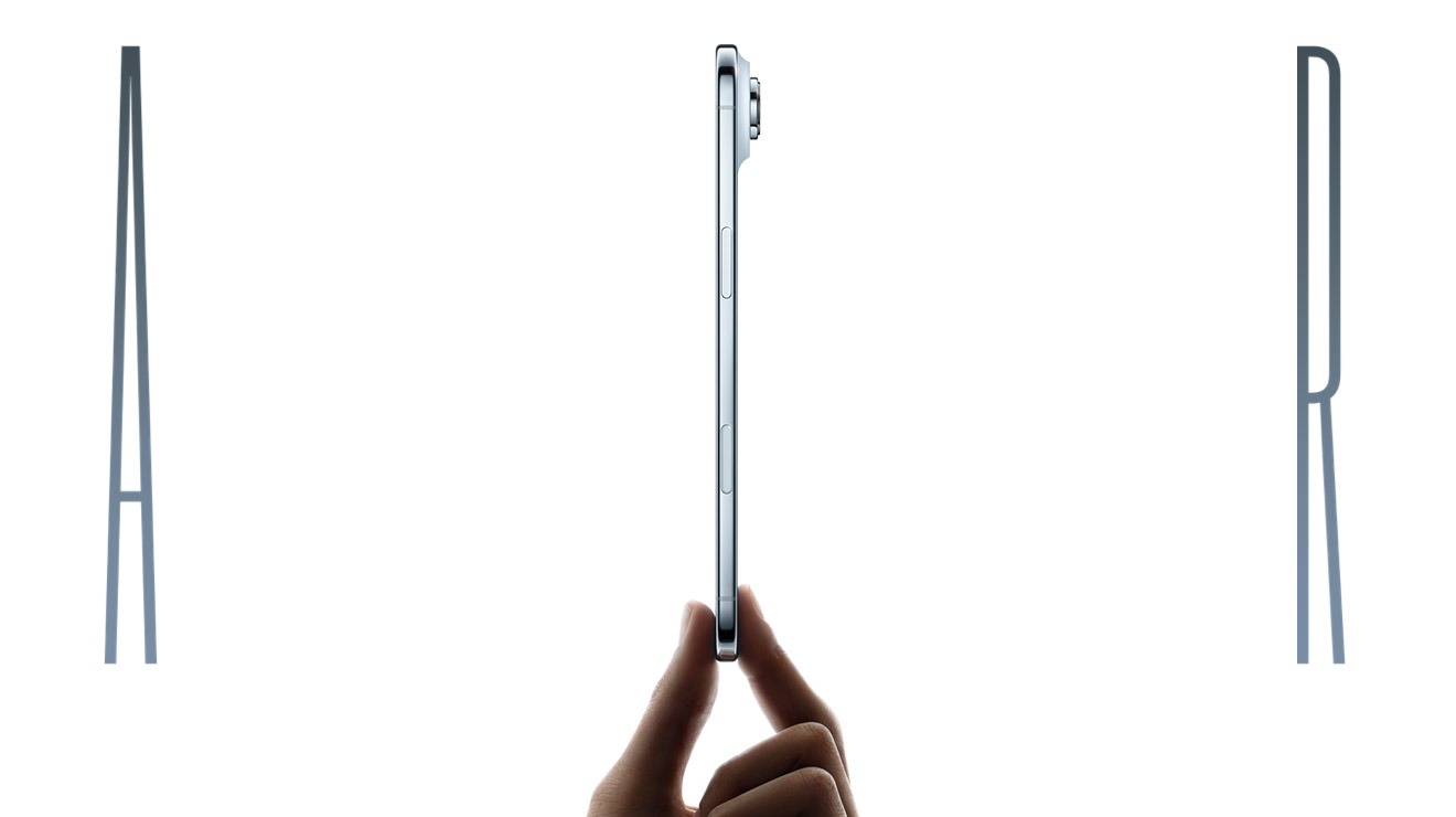 The word Air, spelled in thin chrome-colored letters. The I in Air is a side view of an iPhone Air device in Cloud White being held upright between the thumb and pointer finger of a hand. The side view of the iPhone Air shows a button and part of a camera peeking out from the top right.