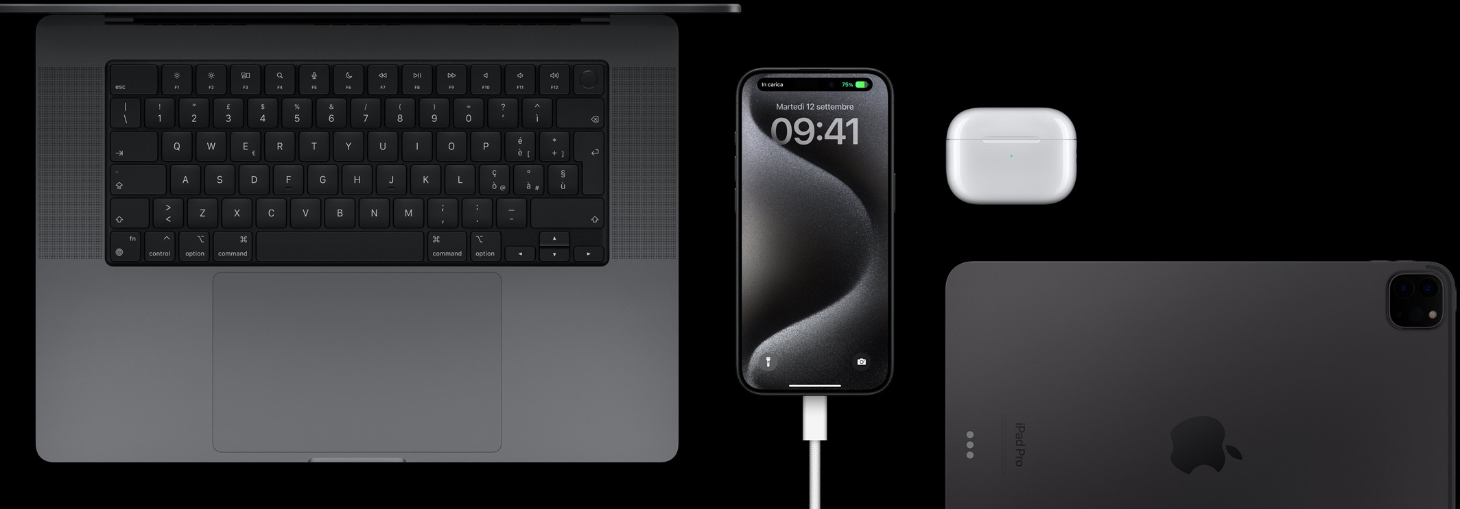 Un iPhone 15 Pro collegato a un cavo USB-C con intorno un MacBook Pro, un paio di AirPods Pro e un iPad