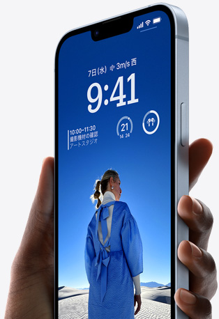 片手に持たれたブルーのiPhone 14。ロック画面はカスタマイズされていて、青い服を着た人物の写真が映し出され、時刻とウィジェットが表示されている。