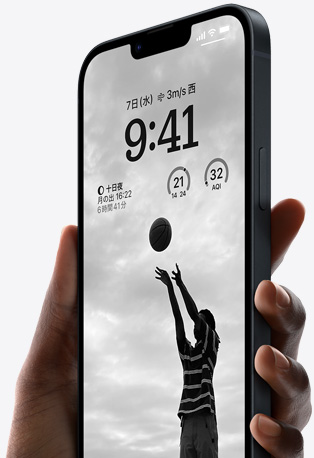 片手に持たれたミッドナイトのiPhone 14。ロック画面はカスタマイズされていて、バスケットボールをしている人物の写真が映し出され、フォントは黒。ウィジェットも見えている。