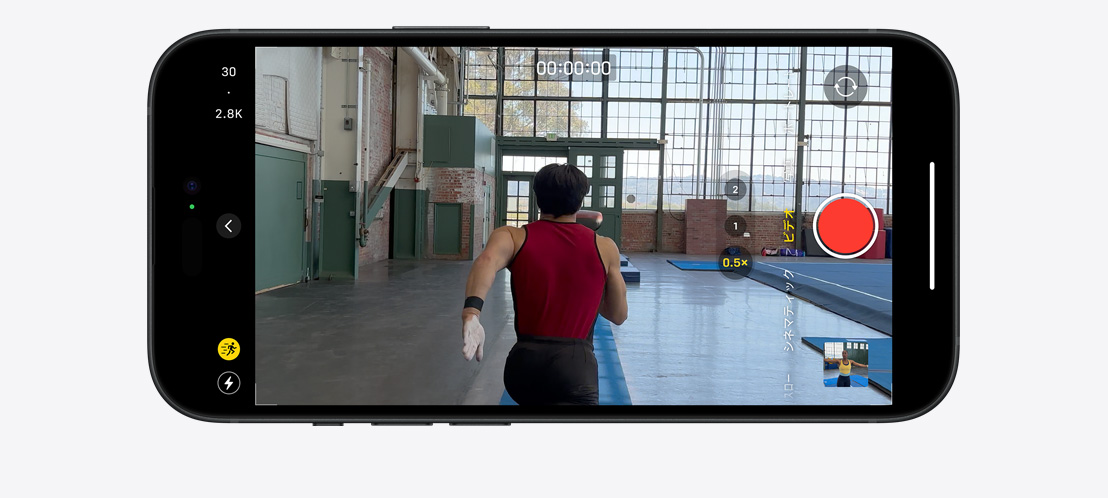明るく大きな体育館を駆ける体操選手のビデオをアクションモードで撮影しているiPhone 15 Proの画像。