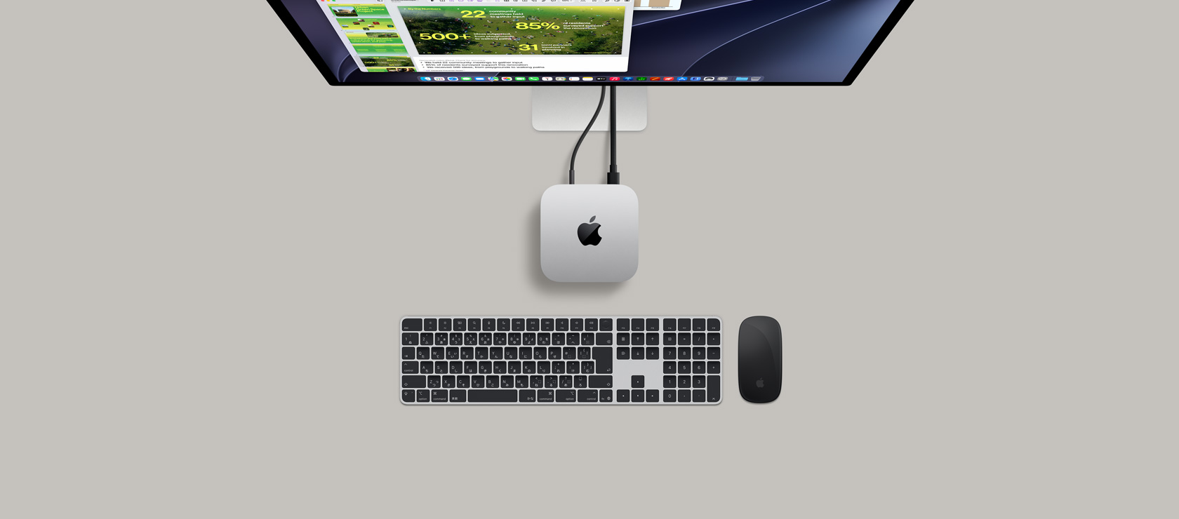 Mac miniを上から見た図。シルバーのアルミニウム、丸みを帯びた四隅、中央に光沢のあるブラックのAppleのロゴ。コードで接続されている。上部にStudio Displayの一部分が見えており、画面にカレンダーアプリ、Keynoteのプレゼンテーション、棒グラフが表示されている。Mac miniの下にテンキーが付いたMagic KeyboardとMagic Mouseが見えている