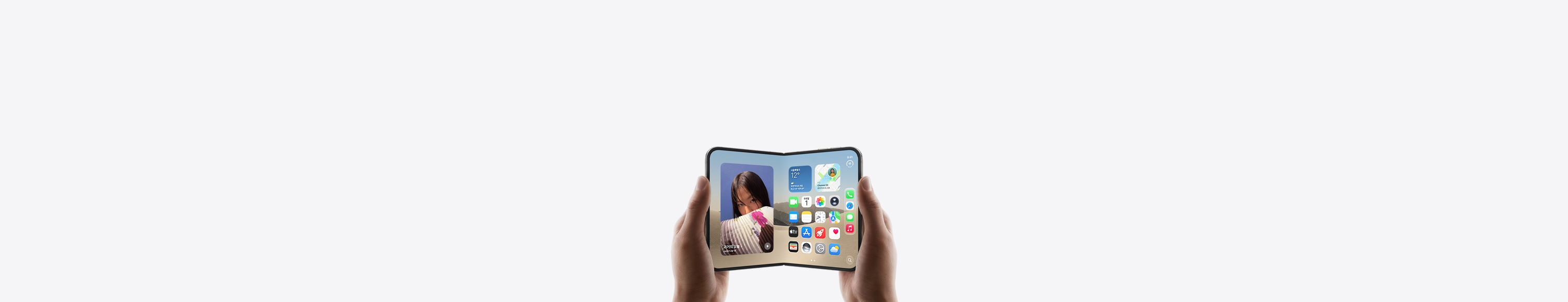 iPhone Duo를 가로 방향으로 펼친 상태에서 두 손으로 들고 있는 모습. 내부 디스플레이에 홈 화면이 보입니다.