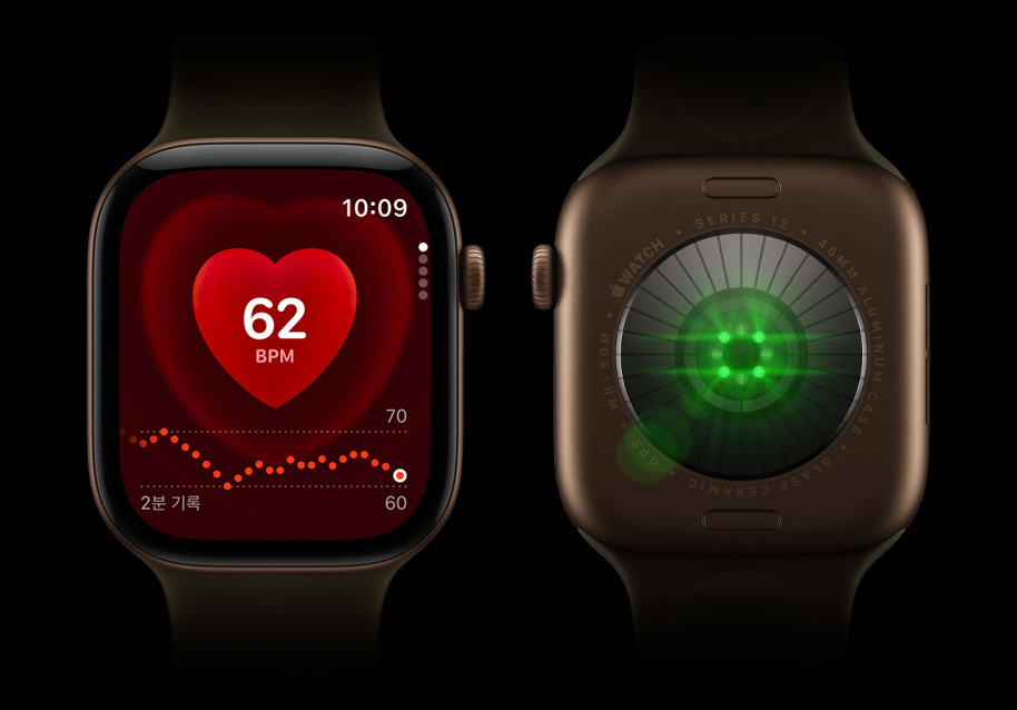 나란히 놓인 Apple Watch Series 12 두 대. 뒷면 크리스털에는 밝은 초록색 센서 불이 켜져 있고, 앞면에는 심박수 모니터가 표시된 디스플레이가 보입니다.