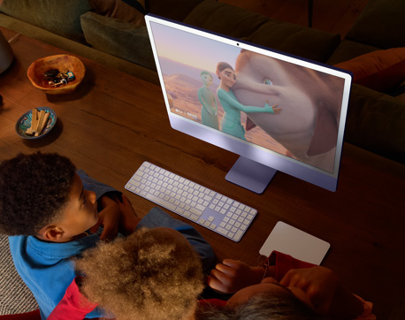 젊은 세 사람이 iMac, Magic Keyboard, Magic Trackpad가 놓여 있는 테이블에 앉아 영화를 보고 있는 모습