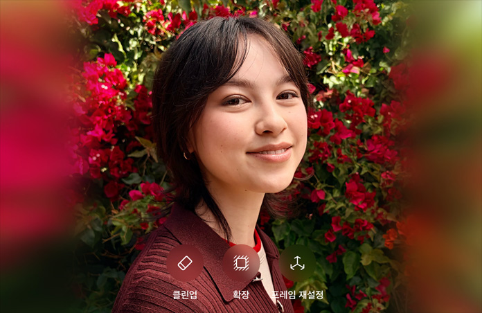 갈색 스웨터를 입고 웃고 있는 갈색 머리의 사람을 빨간색 꽃이 둘러싸고 있는 사진. 사진 위에 AI 사진 편집 기능인 클린업, 확장, 프레임 재설정 옵션이 표시되어 있습니다.