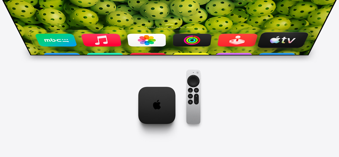 جهاز Apple TV 4K وريموت Apple TV تحت شاشة تلفزيون، الشاشة تعرض أيقونات تطبيقات في الصف العلوي من الشاشة الرئيسية على خلفية كرات بيكلبول خضراء اللون