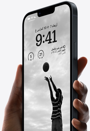 يد تحمل iPhone 14 بلون سماء الليل تظهر عليه شاشة قفل مخصصة تضم صورة شخص يلعب كرة السلة، وخطاً باللون الأسود، وأدوات بارزة